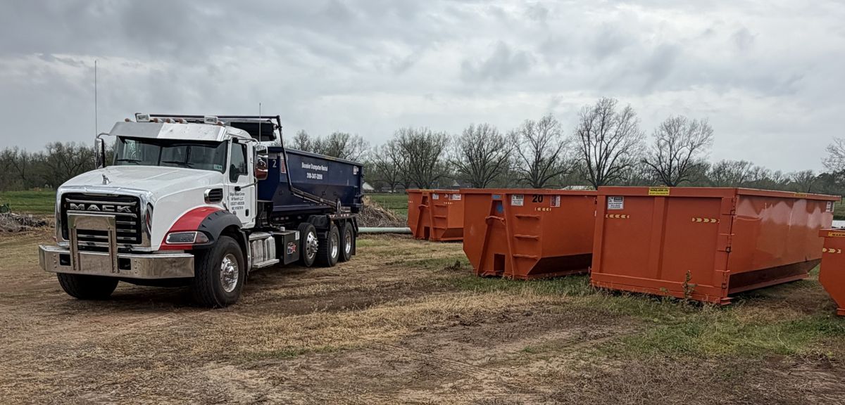 Mack roll-off truck with blue and orange Bossier Dumpster Rental containers at the yard