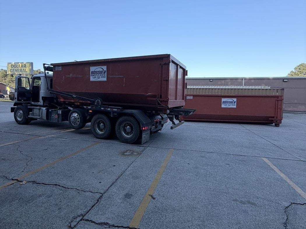 Roll-off truck hauling a Bossier Dumpster Rental container out of a Shreveport commercial lot