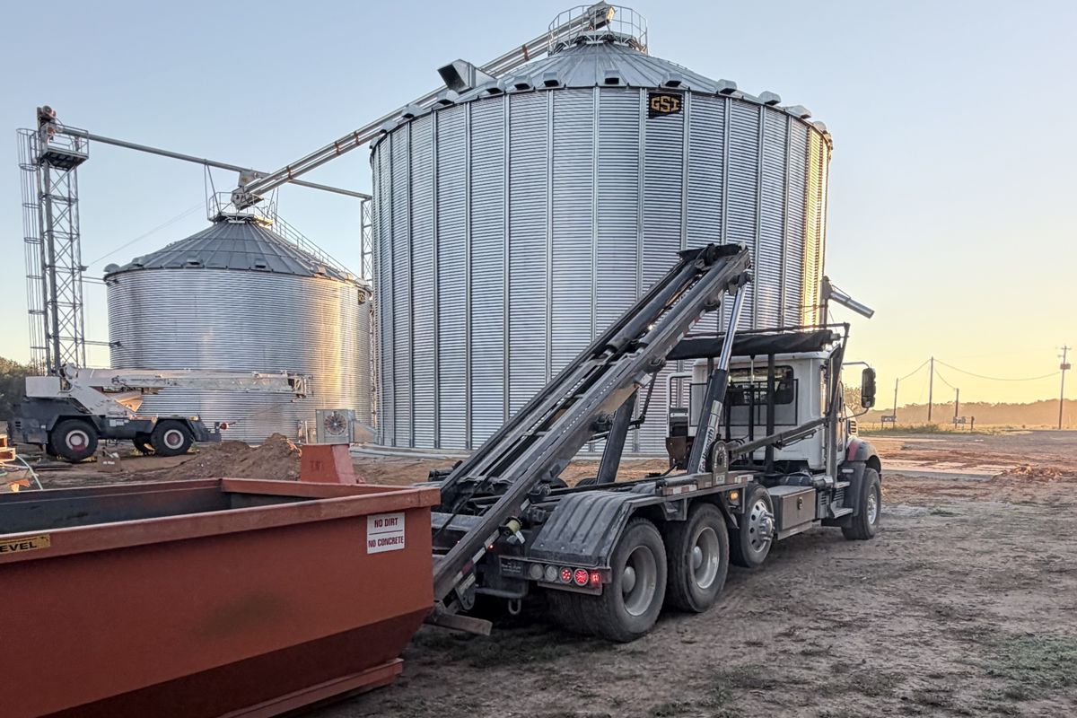 Roll-off truck dropping a dumpster at a grain bin construction site at sunrise