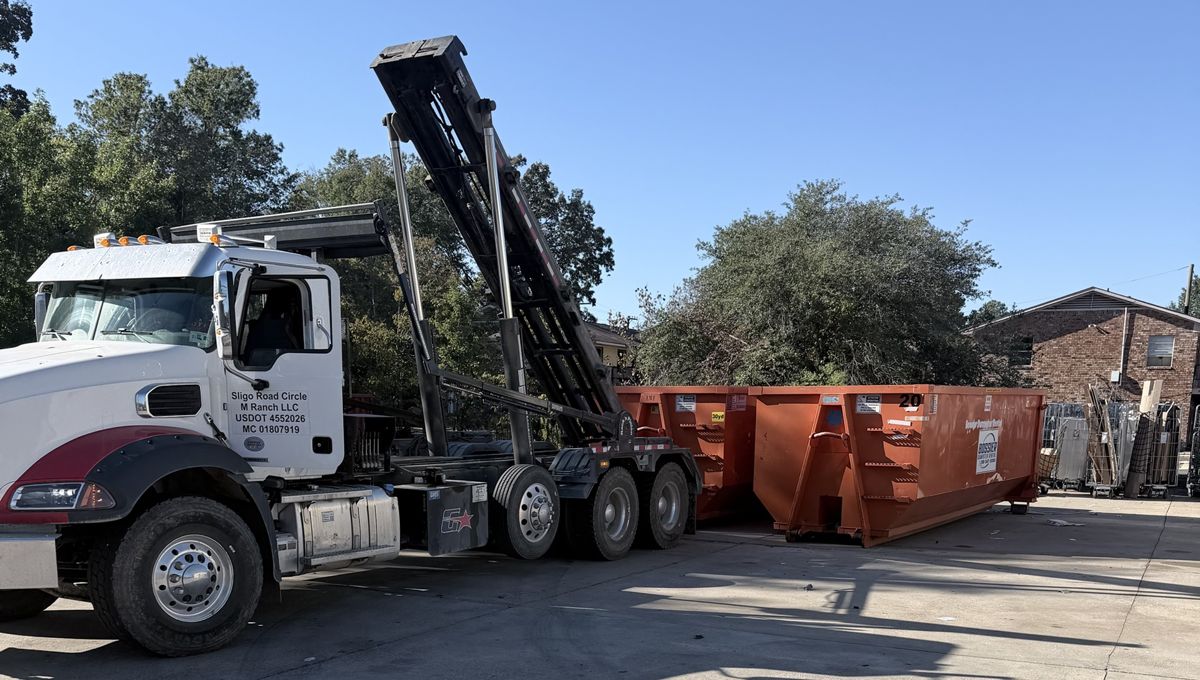 Mack roll-off truck staging orange 20 and 30-yard dumpsters at a Shreveport commercial site